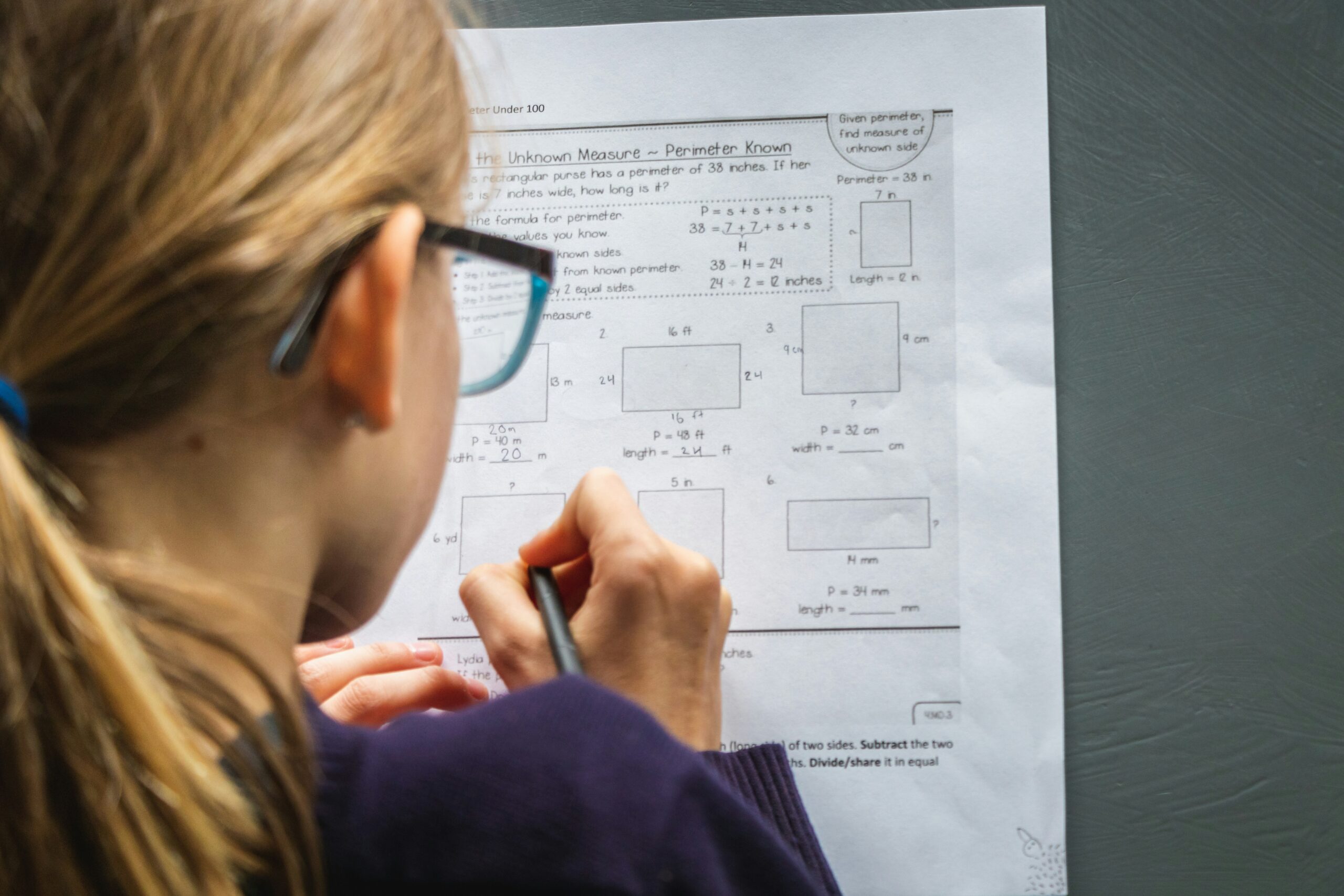 A Young Girl working on a math worksheet. She wears glasses and a purple sweatshirt. She is a change maker in progress.