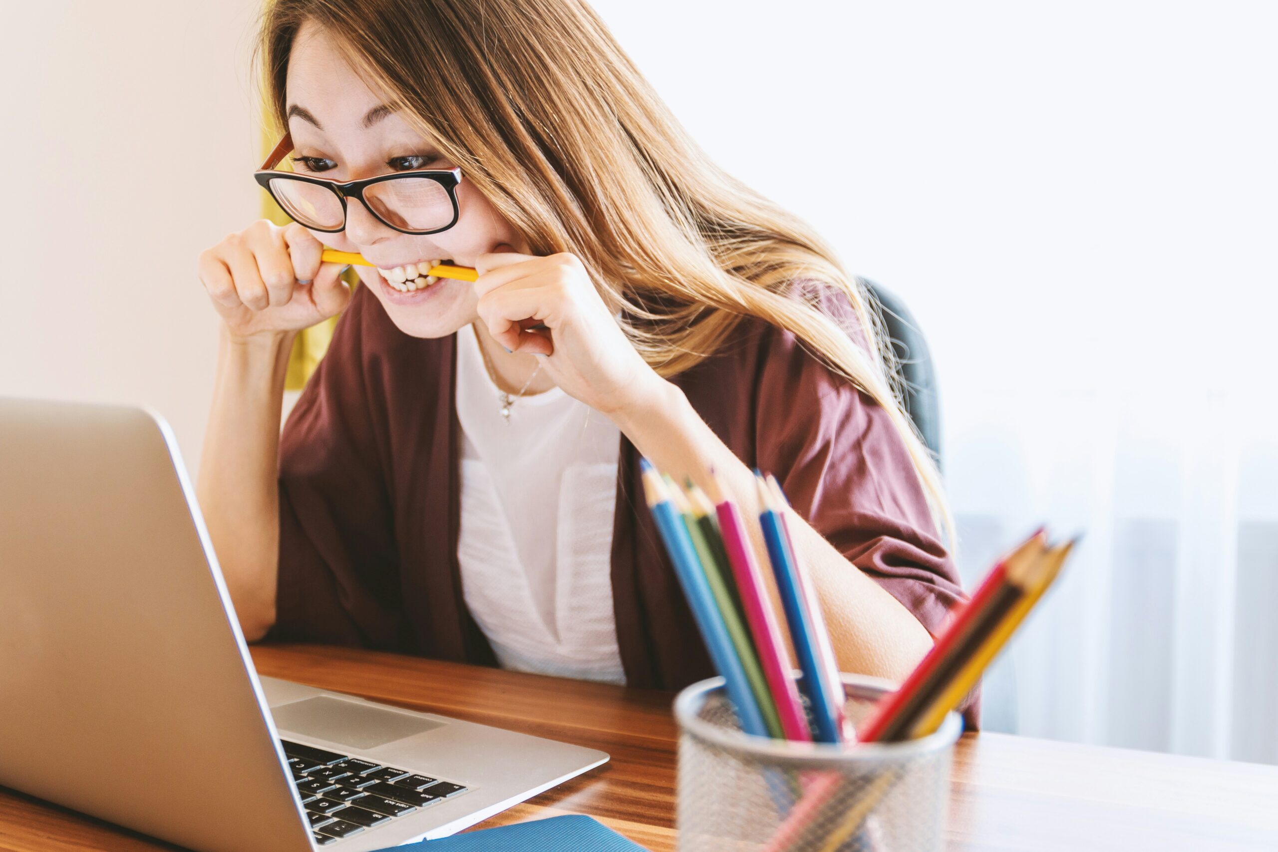 A Woman in a purple shaw and glasses bites her pencil as she stairs at her computer, stress and burnout threaten her ability to keep it together at work.